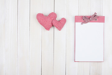 Notebook and hearts on white wood background