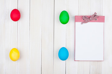 Easter eggs and notebook on white wood background