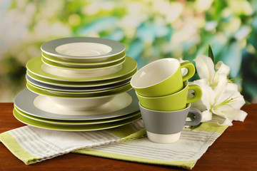 Empty plates and cups on wooden table on green background