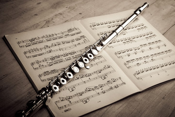 Silver flute on an ancient music score background - obrazy, fototapety, plakaty
