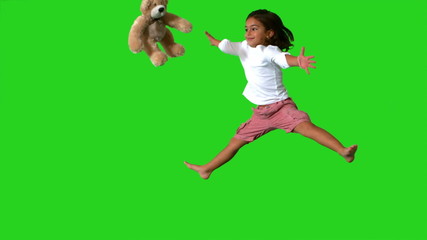 Little girl jumping on green screen and catching teddy