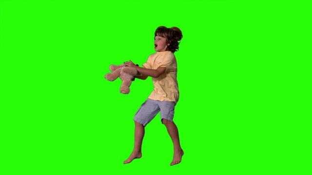Young boy jumping up and catching teddy bear on green screen