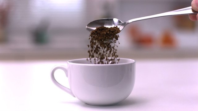 Pouring instant coffee from teaspoon into a white cup