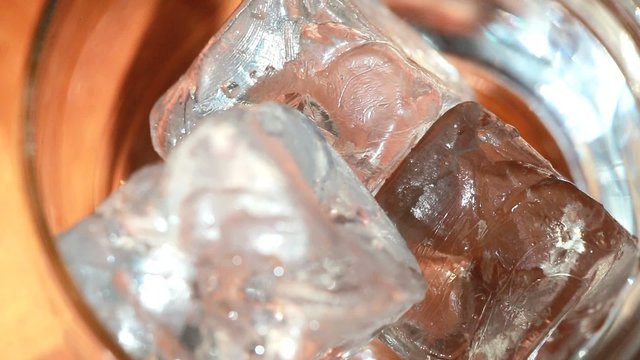 Tongs Placing Ice Into Tumbler And Whiskey Being Poured Over