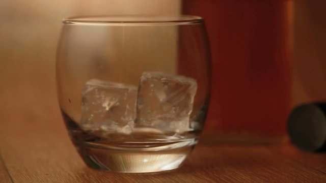 Tongs placing ice into tumbler and whiskey being poured