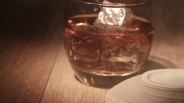 Cigar being placed beside tumbler of whiskey on the rocks