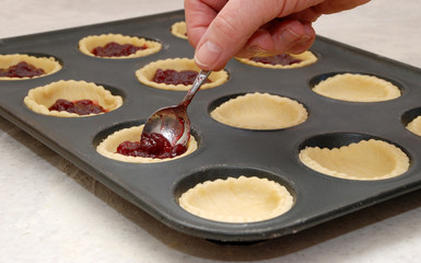 A woman's hand holding a teaspoon as she fills jam tarts