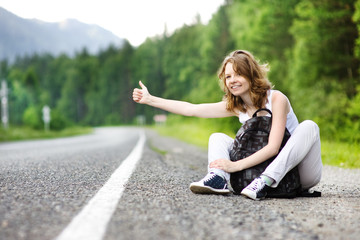 Young smiling woman with backpack catching a car on empty road
