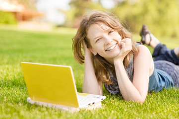 college student lying down on the grass working on laptop