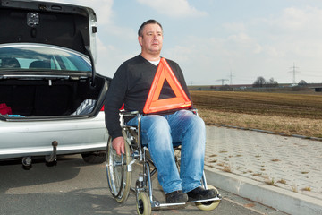 Man in a wheelchair and warning triangle next to his car