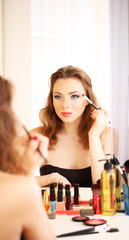 Young beautiful woman making make-up near mirror