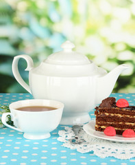 Teapot, cup of tea and delicious cake on natural background