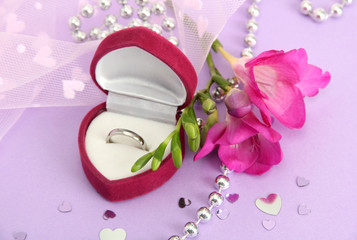 Beautiful box with wedding ring and flower on purple background