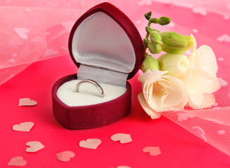 Beautiful box with wedding ring and flower on pink background