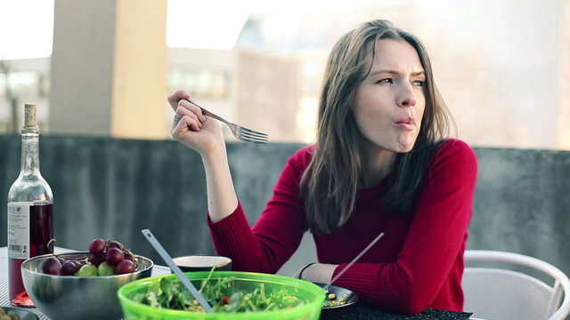 Pensive woman eating salad and drinking tea on terrace