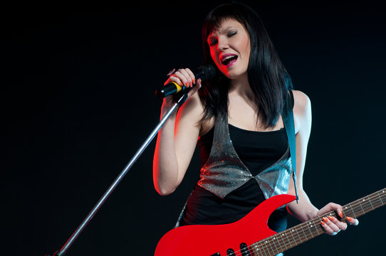 Young rock woman holding a guitar and singing with a microphone