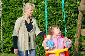 A mother playing with her baby in a swing