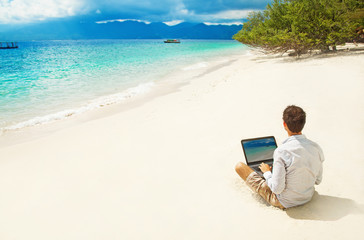 man with laptop on colorful beach of island