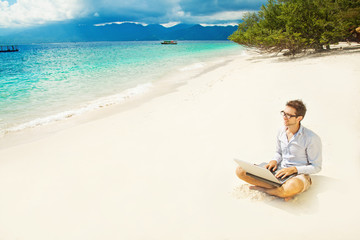 man with laptop on colorful beach of island