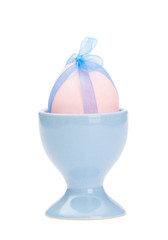 Pink colored easter egg  with blue ribbon is in blue egg cup