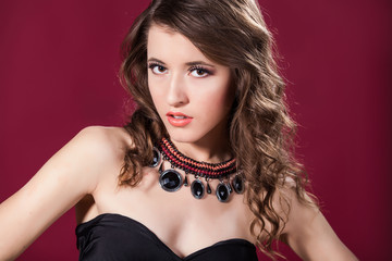 beautiful young woman with jewelry on neck over red background