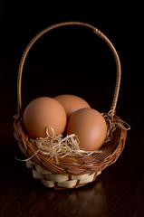 Easter eggs in the basket of hay on a wooden, dark brown table