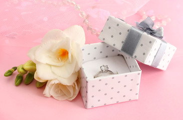 Beautiful box with wedding ring and flower on pink background