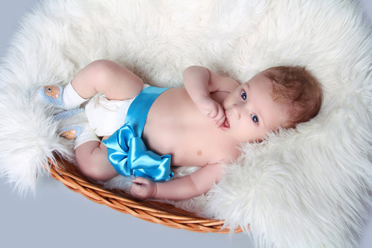 Portrait Of Newborn Baby Lying On Fur With Blue Bow In Bed