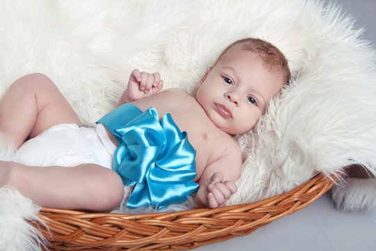 Portrait Of Newborn Baby Lying On Fur With Blue Bow In Bed