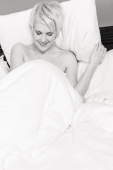 Obraz na płótnie Canvas Monochrome image of a smiling woman sitting in a hotel bed