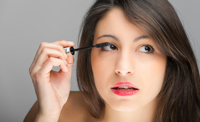 Pretty young woman applying mascara using lash brush