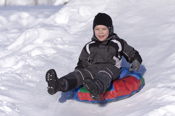 Fototapeta na wymiar Szczęśliwy chłopak slide w dół wzgórza. Zimna zima.
