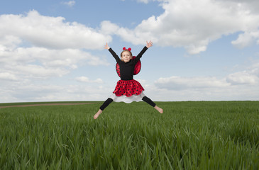 little girl in lady bug costume jumping in the fileds