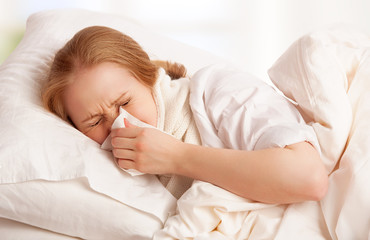 ill sick young woman sneezes  into a handkerchief in bed