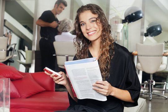 Woman With Mobile Phone And Magazine At Hair Salon