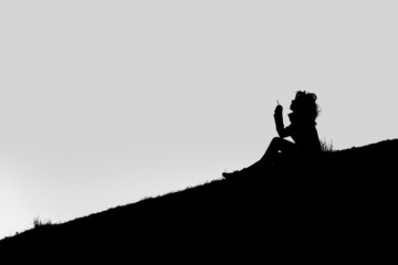 A Silhouette of a girl seated on the ground, smoking