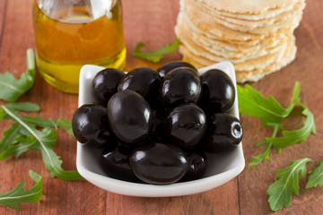 black olives in white bowl with oil and toasts
