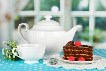 Teapot, cup of tea and delicious cake on window background