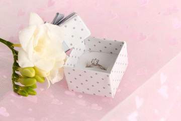 Beautiful box with wedding ring and flower on pink background