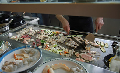 chef prepares dishes with vegetables and meat cooked on a griddl