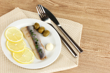 Dish of herring and lemon on plate on wooden table close-up
