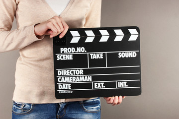 Movie production clapper board in hands on grey background