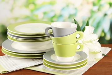 Empty plates and cups on wooden table on green background