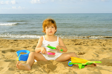 Happy toddler girl playing with her toys at beach