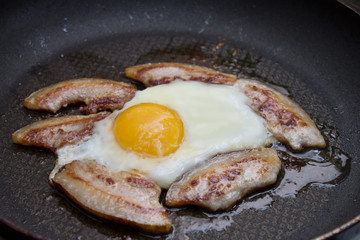 Bacon and eggs cooking in a skillet