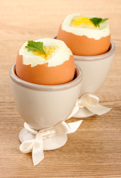 Boiled eggs in egg cups, on wooden table