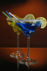 Yellow and blue cocktails in glasses on color background