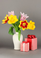 Beautiful tulips in bucket with gifts on grey background