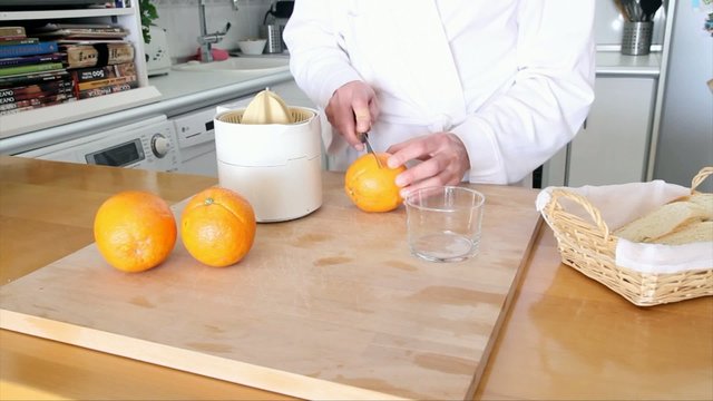 Mujer en bata blanca preparando zumo de naranja por la mañana en la cocina