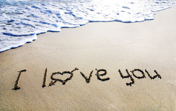 words "I love you" outline on the wet sand with the wave brillia